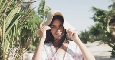 Güneşli sahilde gülümseyen, güneşli şapkalı ve güneşli elbiseli mutlu İspanyol kadın portresi, yavaş çekim. Yaz, dinlenme ve tatiller.