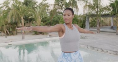 Çift ırklı mutlu kadın yoga yapıyor, kollarını kumsala uzatmış, ağır çekimde duruyor. Yaz, rahatlama, sağlıklı yaşam tarzı ve tatiller..