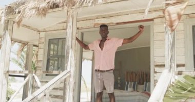Afrika kökenli Amerikalı bir adam sabah güneşinde ahşap sahil evinin verandasında geriniyor, ağır çekimde. Yaz, dinlenme ve tatiller.