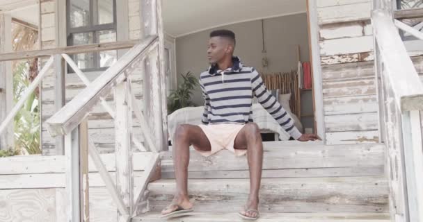 Afrykański Amerykanin Siedzący Schodach Drewnianego Domku Plaży Relaksujący Się Słońcu — Wideo stockowe