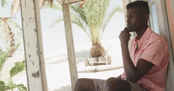 Przemyślany Afrykanin Siedzący Ganku Drewnianego Domku Plaży Patrzący Zwolnionym Tempie — Wideo stockowe