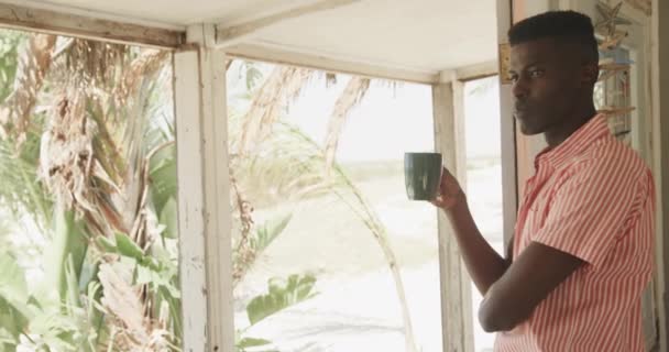 Przemyślany Afroamerykanin Pijący Kawę Drzwiach Domku Plaży Spowolniony Ruch Lato — Wideo stockowe