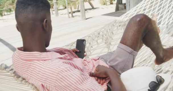 Afrykański Amerykanin Leżący Hamaku Używając Smartfona Słonecznej Plaży Zwolnionym Tempie — Wideo stockowe