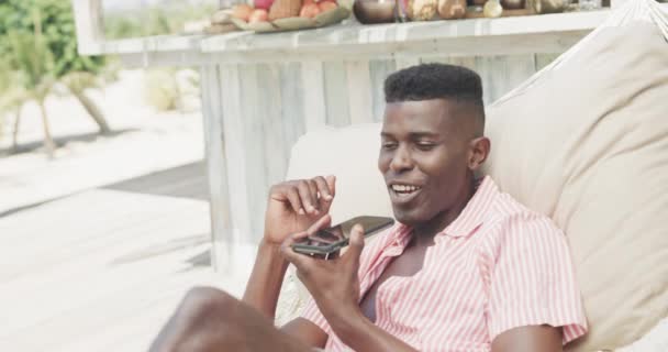 Щасливий Афроамериканець Який Сидить Гамаку Розмовляє Смартфону Сонячному Пляжі Сповільнюючи — стокове відео
