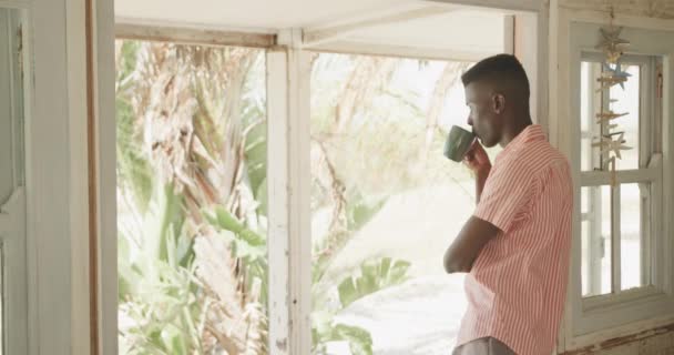 Przemyślany Afroamerykanin Pijący Kawę Drzwiach Domku Plaży Spowolniony Ruch Lato — Wideo stockowe