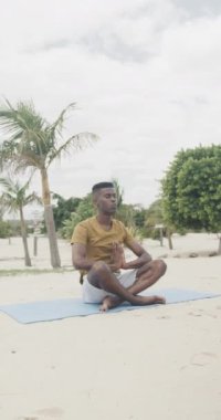 Afrika kökenli Amerikalı bir adamın yoga meditasyonu uyguladığı dikey video, yavaş çekim. Yaz, rahatlama, sağlıklı yaşam tarzı ve tatiller..