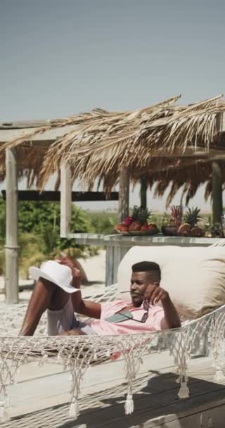 Pionowe Wideo Afrykańskiego Amerykanina Hamaku Przykrywającego Twarz Kapeluszem Słonecznej Plaży — Wideo stockowe
