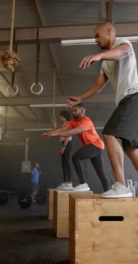 Spor salonundaki çeşitli sporcuların yavaş çekimde kutulara atladığı dikey bir video. Yaşam tarzı, fitness, aktivite ve güven.