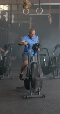 Spor salonunda yavaş çekimde eliptik bisiklet kullanan melez bir sporcunun dikey videosu. Yaşam tarzı, fitness, aktivite ve güven.