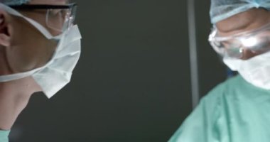 Ameliyat odasında ameliyat sırasında maskeli çeşitli cerrahlar ağır çekimde konuşuyor. İlaç, sağlık ve bakım.