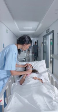Melez bir kadın doktorla yatakta kızın hastanede ağır çekimde konuştuğu dikey bir video. İlaç, sağlık ve bakım.