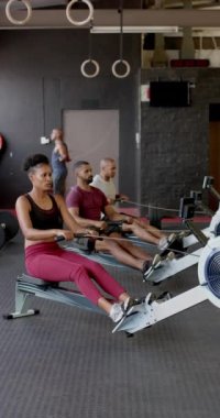 Spor salonundaki kürek makinelerini yavaş çekimde kullanan sporcuların dikey videosu. Yaşam tarzı, fitness, aktivite ve güven.