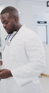 Ağır çekimde tablet kullanan mutlu Afro-Amerikan erkek doktorun dikey portresi. Tıp, sağlık, teknoloji ve bakım.