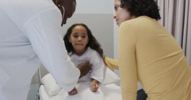 Doktorlar, ağır çekimde annesiyle birlikte steteskoplu bir kızı muayene ediyorlar. İlaç, sağlık ve bakım.