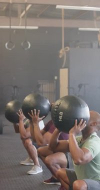 Sporcuların spor salonunda ağır çekimde ilaç toplarını kaldırdığı dikey bir video. Yaşam tarzı, fitness, aktivite ve güven.