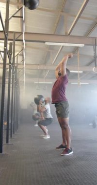 Sporcuların spor salonunda ağır çekimde ilaç toplarını kaldırdığı dikey bir video. Yaşam tarzı, fitness, aktivite ve güven.