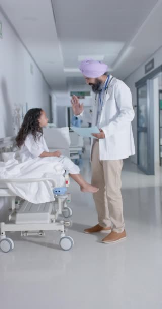 在医院里 男性医生与女孩在床上高举双手慢动作的垂直录像 保健和护理 — 图库视频影像