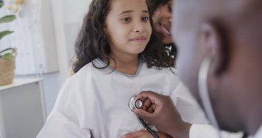 Annesiyle birlikte ağır çekimde steteskopla hasta kızı muayene eden mutlu doktor. İlaç, sağlık ve bakım.