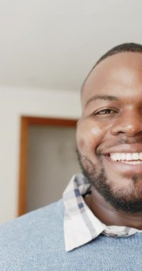 Afrikalı Amerikalı bir adamın kameraya bakıp ağır çekimde gülümsemesinin dikey videosu. Yaşam tarzı ve ev hayatı.