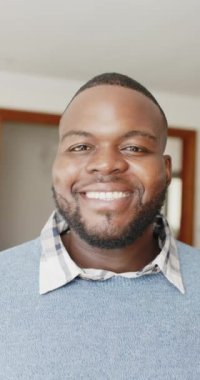 Afrikalı Amerikalı bir adamın kameraya bakıp ağır çekimde gülümsemesinin dikey videosu. Yaşam tarzı ve ev hayatı.