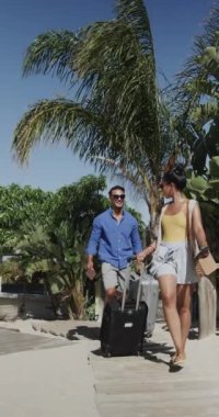 Güneşli sahile bavullarıyla gelen mutlu çiftin dikey videosu, yavaş çekim. Seyahat, rahatlama, tatil ve yaşam tarzı.