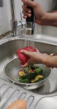 Afro-Amerikan kadının sebzeleri yavaş çekimde yıkarken çekilmiş dikey videosu. Ev hayatı ve yiyecek..