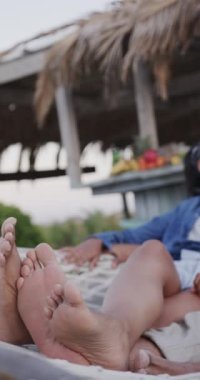 Hamakta uzanmış plaj barında ağır çekimde konuşan mutlu çiftin dikey videosu. Rahatlama, romantizm, tatiller ve yaşam tarzı.