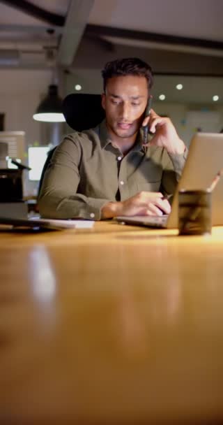 Вертикальное Видео Латиноамериканского Бизнесмена Использующего Ноутбук Разговаривающего Смартфоне Офисе Замедленная — стоковое видео
