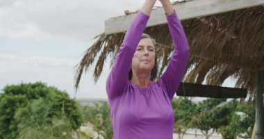 Kumsalda yoga meditasyonu yapan son sınıf beyaz kadın. Ağır çekimde. Emeklilik, dinlenme, tatiller ve sağlıklı yaşlı yaşam tarzı..