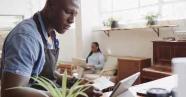 Afro-amerikan erkek barista tablet kullanıyor ve kahve dükkanında dokümanları tutuyor, ağır çekimde. Yaşam tarzı, iletişim, girişimcilik ve yerel işletme.