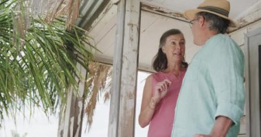 Ahşap sahil evinin verandasında konuşan yaşlı beyaz çift yavaş çekimde manzaranın tadını çıkarıyorlar. Emeklilik, dinlenme, tatiller ve sağlıklı yaşlı yaşam tarzı..