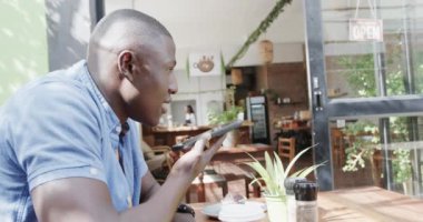 Kafede akıllı telefondan konuşan mutlu Afro-Amerikan adam, ağır çekimde. Yaşam tarzı, iletişim, girişimcilik ve yerel işletme.
