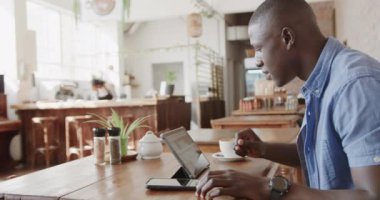 Mutlu Afro-Amerikan adam tablet kullanıyor ve kahvesini ağır çekimde içiyor. Yaşam tarzı, iletişim, girişimcilik ve yerel işletme.