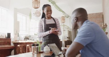 Afro-Amerikalı bayan barista kahve dükkanında müşteriden sipariş alıyor, ağır çekimde. Yaşam tarzı, iletişim, girişimcilik ve yerel işletme.