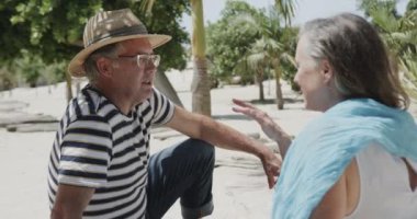 Kumsalda oturan ve ağır çekimde konuşan Kafkasyalı mutlu çift. Emeklilik, rahatlama, tatiller ve yaşlı yaşam tarzı.