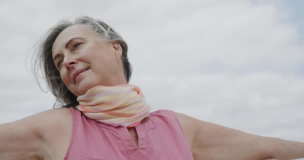 ゆっくりとした動きで 曇った空に向かって笑顔を伸ばして腕を持つ幸せなシニア白人女性 リラクゼーション アクティブなシニアライフスタイル — ストック動画