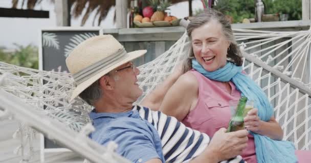 幸せな高齢者の白人のカップルを飲むとビーチバーの外のハンモックで ゆっくりと動きで話しています リラクゼーション ロマンス シニアライフスタイル — ストック動画