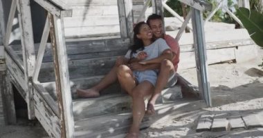 Tahta sahil evinin merdivenlerinde ağır çekimde birbirine sarılan mutlu çift. Rahatlama, romantizm, tatiller ve yaşam tarzı.