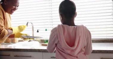 Mutlu Afro-Amerikan anne ve kızı mutfakta bulaşık yıkıyor, ağır çekimde. Yaşam tarzı, birliktelik, aile ve aile hayatı..