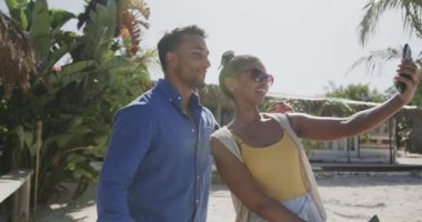 Mutlu çift gülüyor ve yavaş çekimde Sunny Beach 'te akıllı telefonuyla selfie çekiyor. Rahatlama, romantizm, tatiller, iletişim ve yaşam tarzı.