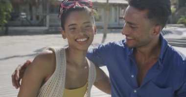 Güneşli sahilde ağır çekimde oturan mutlu çift kucaklaşması. Rahatlama, romantizm, tatiller ve yaşam tarzı.