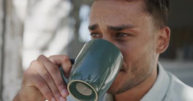 Çift ırklı mutlu bir adam, sahil evinin verandasında ağır çekimde kahve içiyor. Rahatlama, tatiller ve yaşam tarzı.