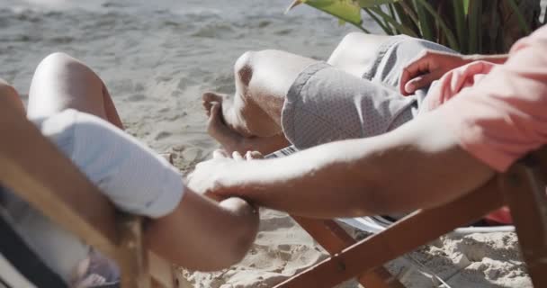 Šťastný Různorodý Pár Sedící Lehátkách Držící Ruce Pláži Slunci Zpomaleném — Stock video