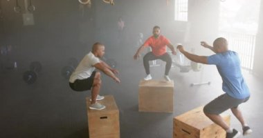 Çeşitli erkek fitness sınıfları kutuların üstüne atlıyor, spor salonunda ağır çekimde çapraz antrenman yapıyor. Sağlıklı yaşam tarzı, çapraz eğitim, fitness, motivasyon, güç ve egzersiz.
