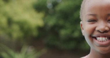 Afrikalı Amerikalı bir kızın portresi gülümseyen ve bahçede kameraya bakan, fotokopi çeken, ağır çekim. Yaşam tarzı, çocukluk ve ev hayatı.