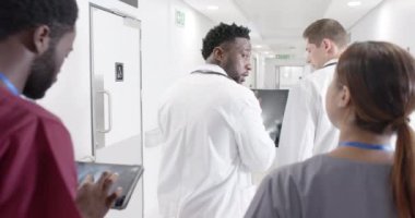 Ciddi çeşitlilikte erkek ve kadın doktorlar röntgen ışınlarıyla konuşuyor ve yürüyorlar, değişmeden. Sağlık, ilaç ve hastane koridoru..