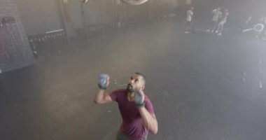 Odaklanmış çift ırklı bir adam spor salonundaki spor salonundaki halkalara yavaş çekimde barfiks çekiyor. Sağlıklı yaşam tarzı, çapraz eğitim, fitness, güç ve egzersiz.