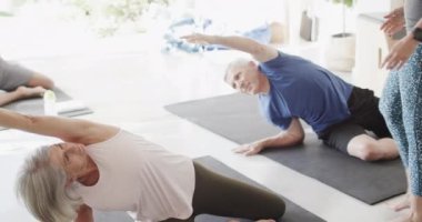 Sunny Room 'da kadın koçla yavaş çekimde, değişmeden pilates yapan çeşitli son sınıf öğrencileri. Egzersiz, emeklilik ve sağlıklı bir yaşam tarzı..