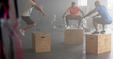 Çeşitli grup fitness sınıfları kutuların üstüne atlıyor, spor salonunda ağır çekimde çapraz antrenman yapıyor. Sağlıklı yaşam tarzı, çapraz eğitim, fitness, motivasyon, güç ve egzersiz.