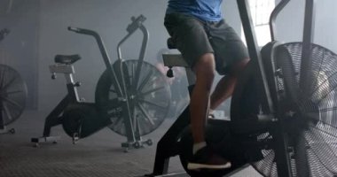 Spor salonunda eliptik bisiklete binen azimli, çift ırklı bir adam, ağır çekimde. Sağlıklı yaşam tarzı, çapraz eğitim, motivasyon, güç ve egzersiz.